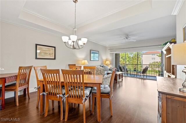 dining area with ornamental molding, ceiling fan with notable chandelier, dark wood-type flooring, and a tray ceiling