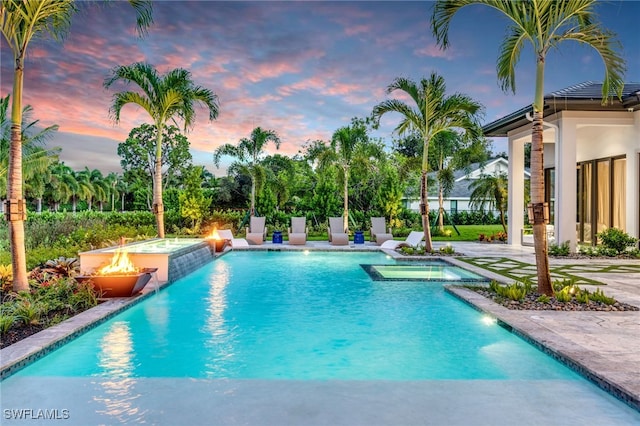 pool at dusk with a fire pit, an in ground hot tub, and pool water feature