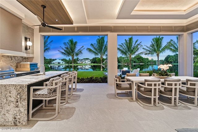 patio terrace at dusk featuring ceiling fan, a water view, a wet bar, and grilling area