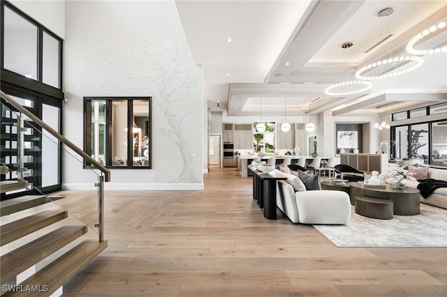 living room with light hardwood / wood-style floors, a raised ceiling, crown molding, and a chandelier