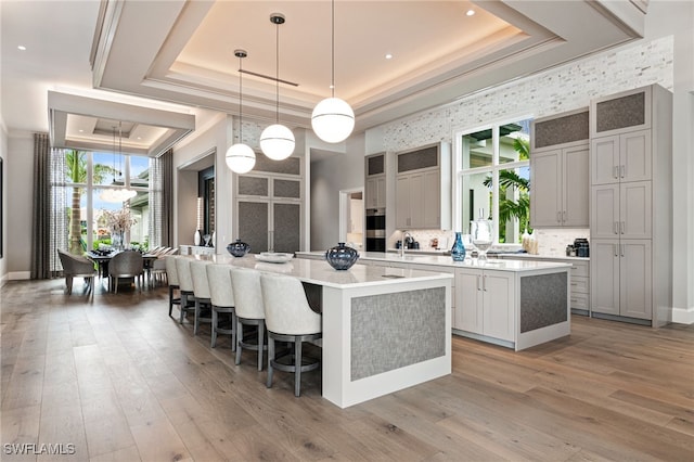 kitchen with a kitchen bar, a raised ceiling, pendant lighting, a center island, and light hardwood / wood-style floors