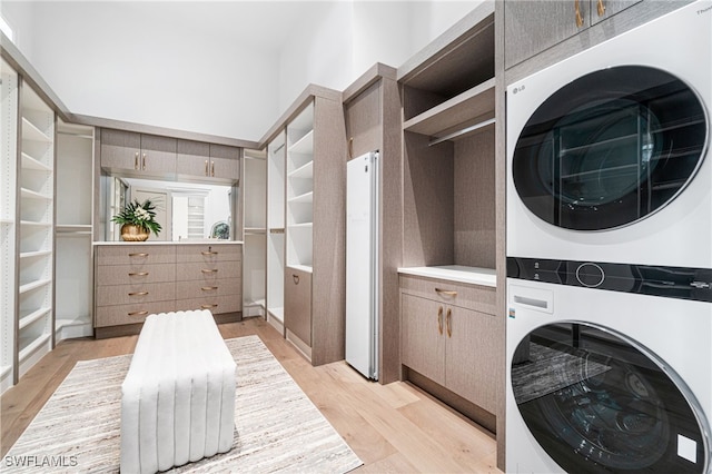 clothes washing area with cabinets, stacked washer / dryer, and light hardwood / wood-style flooring