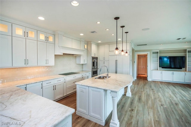 kitchen with light stone counters, white cabinets, hanging light fixtures, a center island with sink, and appliances with stainless steel finishes