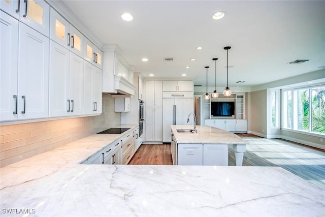 kitchen with white cabinets, pendant lighting, a center island with sink, light hardwood / wood-style flooring, and decorative backsplash