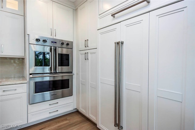 kitchen with double oven, dark hardwood / wood-style flooring, decorative backsplash, and white cabinetry