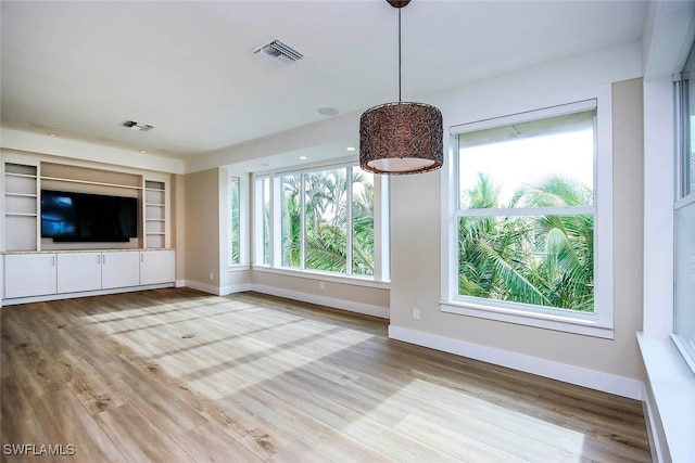 unfurnished living room with built in shelves and light wood-type flooring