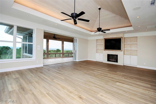 unfurnished living room featuring ceiling fan, wood ceiling, a tray ceiling, a large fireplace, and light hardwood / wood-style floors