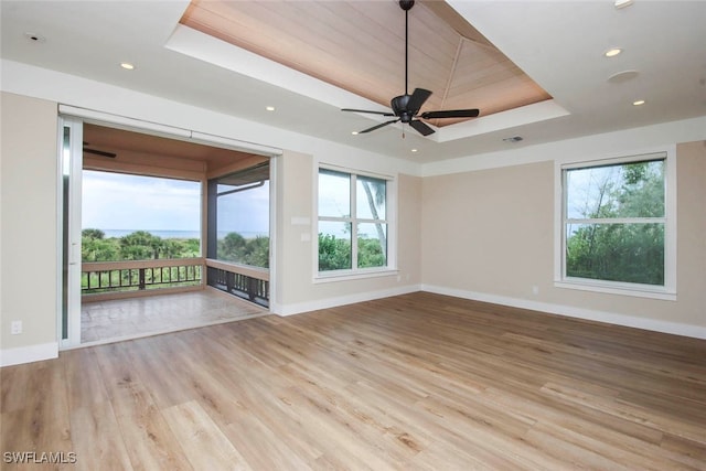 spare room featuring light hardwood / wood-style flooring, ceiling fan, a raised ceiling, and plenty of natural light