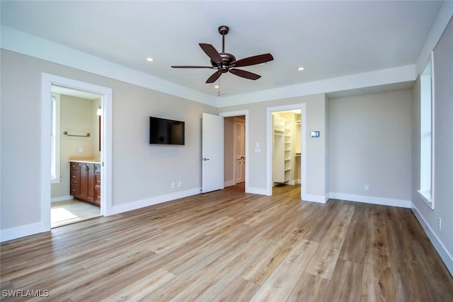 unfurnished bedroom featuring ceiling fan, light hardwood / wood-style floors, ensuite bathroom, and a spacious closet