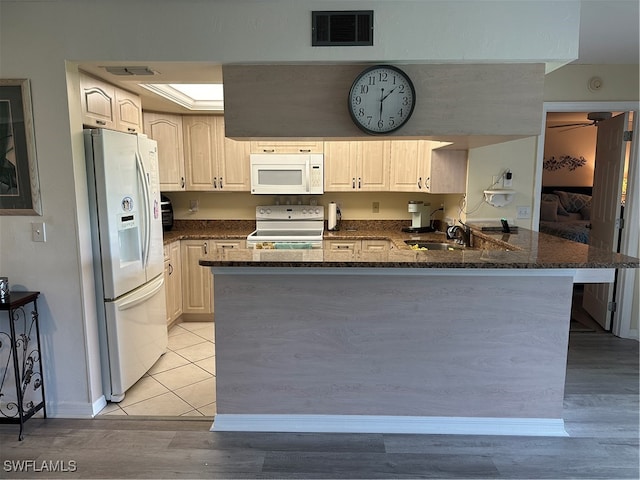 kitchen featuring white appliances, kitchen peninsula, light hardwood / wood-style flooring, dark stone counters, and sink