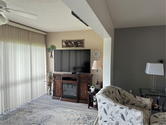 living room featuring a textured ceiling, light hardwood / wood-style floors, lofted ceiling, and ceiling fan