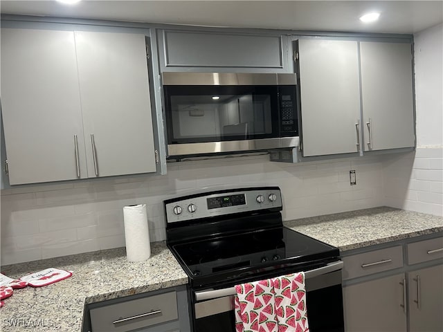 kitchen with gray cabinets, light stone countertops, stainless steel appliances, and tasteful backsplash