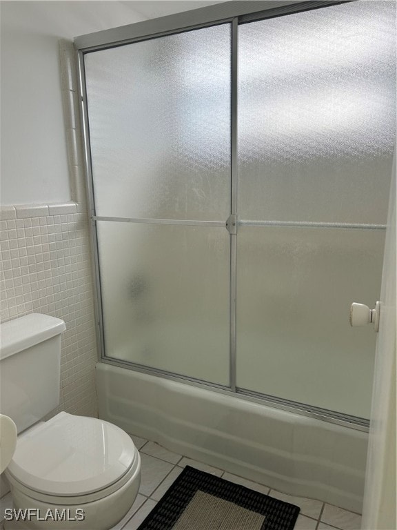 bathroom featuring tile walls, tile patterned flooring, shower / bath combination with glass door, and toilet