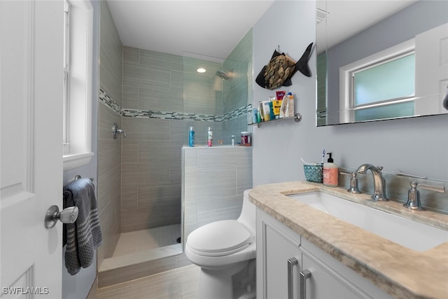 bathroom featuring vanity, a tile shower, wood-type flooring, and toilet