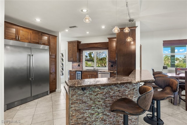 kitchen featuring hanging light fixtures, backsplash, dark stone counters, a breakfast bar, and appliances with stainless steel finishes