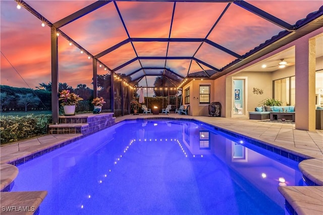 pool at dusk featuring an outdoor living space, ceiling fan, glass enclosure, and a patio area