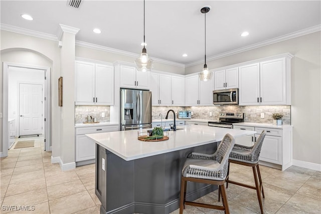 kitchen featuring appliances with stainless steel finishes, white cabinets, decorative backsplash, a kitchen island with sink, and crown molding