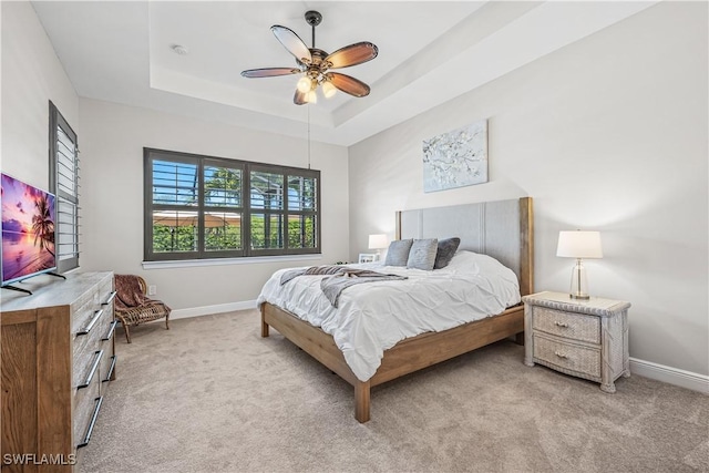 bedroom with light colored carpet, ceiling fan, and a tray ceiling