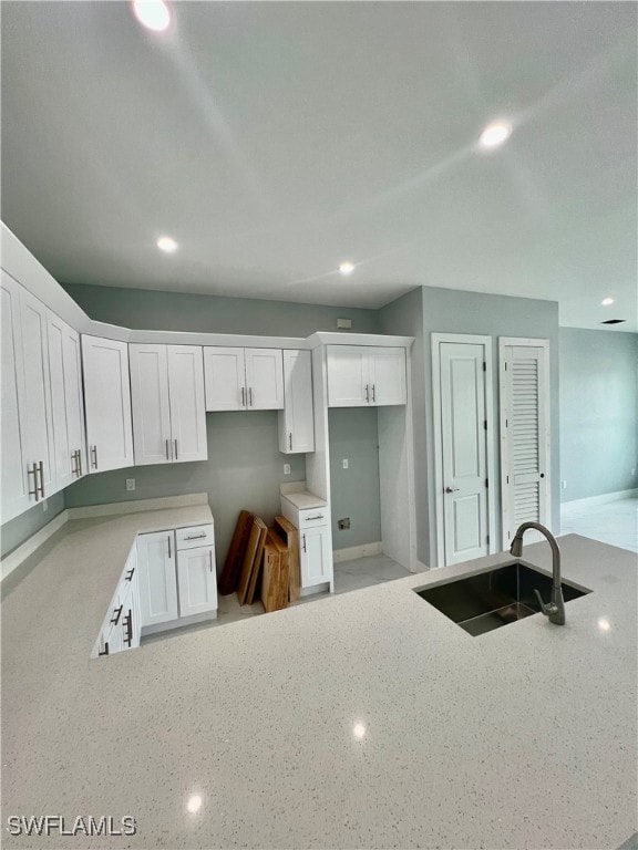 kitchen featuring light stone counters, white cabinets, and sink