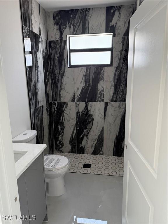 bathroom featuring a tile shower, vanity, and toilet