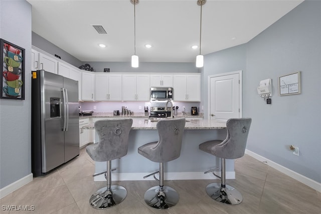 kitchen featuring light stone counters, a kitchen island with sink, white cabinets, hanging light fixtures, and stainless steel appliances