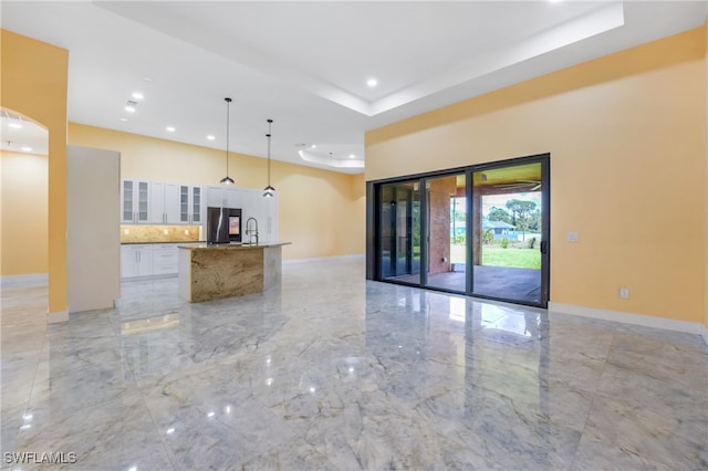 kitchen with white cabinetry, pendant lighting, a tray ceiling, a center island with sink, and sink