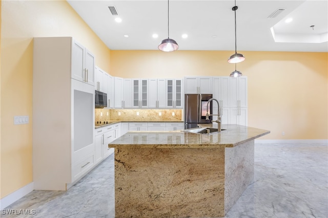 kitchen with white cabinets, a center island with sink, decorative light fixtures, appliances with stainless steel finishes, and light stone countertops