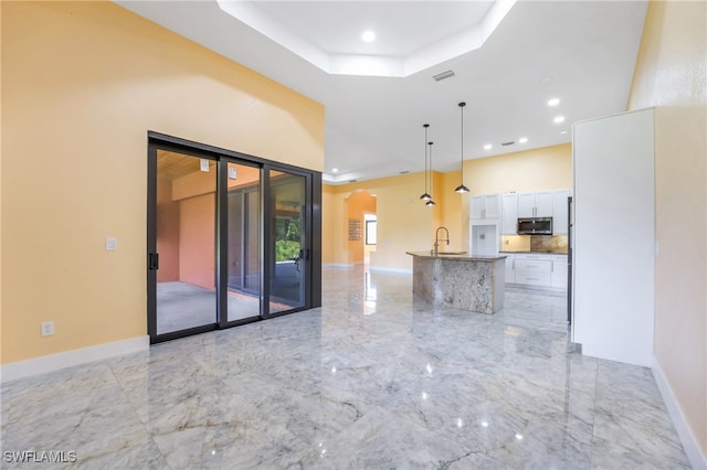 kitchen with white cabinetry, a tray ceiling, decorative light fixtures, and sink