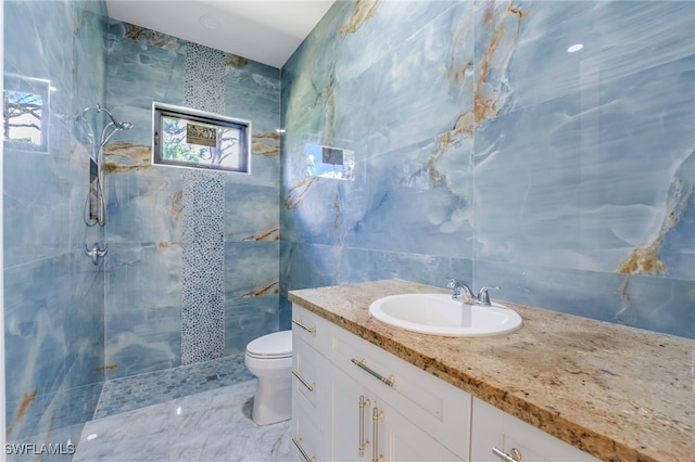 bathroom with tile walls, toilet, vanity, and tiled shower