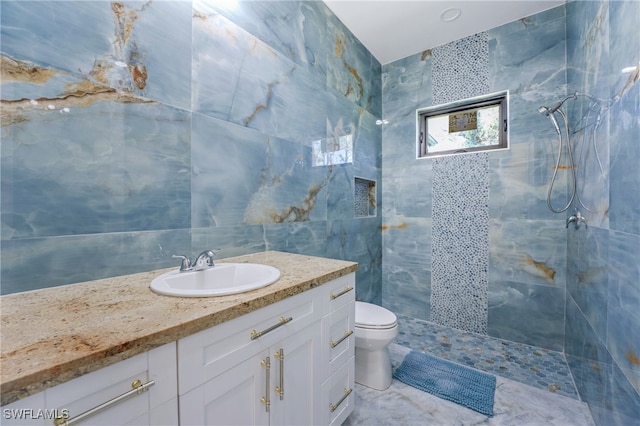 bathroom featuring a tile shower, vanity, tile walls, and toilet