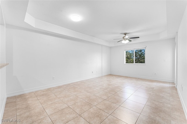 empty room featuring ceiling fan, a raised ceiling, and light tile patterned flooring