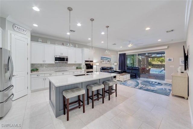 kitchen featuring a center island with sink, light countertops, hanging light fixtures, appliances with stainless steel finishes, and white cabinetry