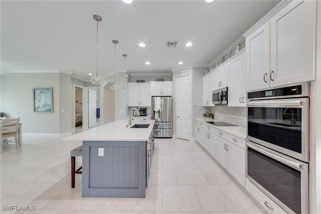 kitchen with pendant lighting, a center island with sink, stainless steel appliances, light countertops, and white cabinetry