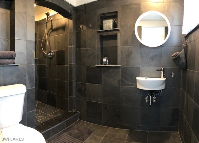 bathroom featuring tile walls, tiled shower, sink, and toilet