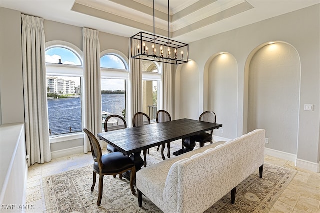 dining space featuring a water view, a notable chandelier, and a raised ceiling