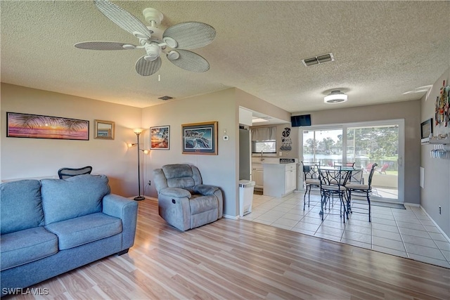 living room with ceiling fan, a textured ceiling, and light hardwood / wood-style flooring