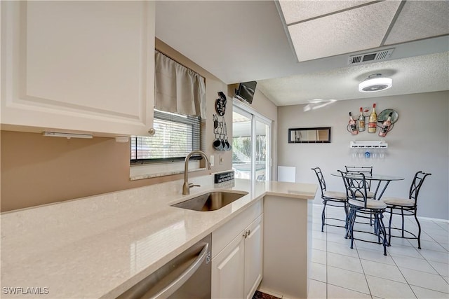 kitchen with white cabinetry, sink, light stone counters, light tile patterned floors, and stainless steel dishwasher