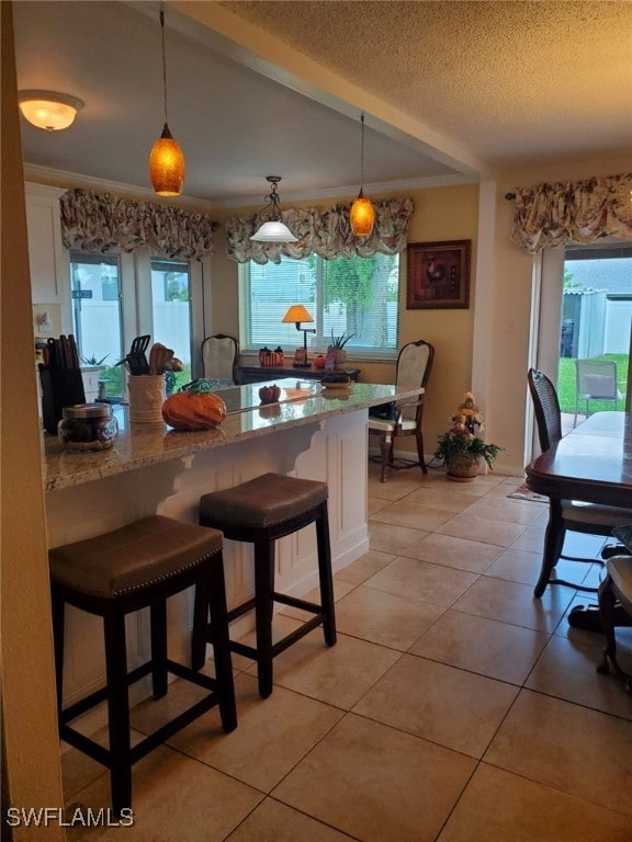 kitchen with light stone counters, hanging light fixtures, a kitchen bar, and white cabinetry