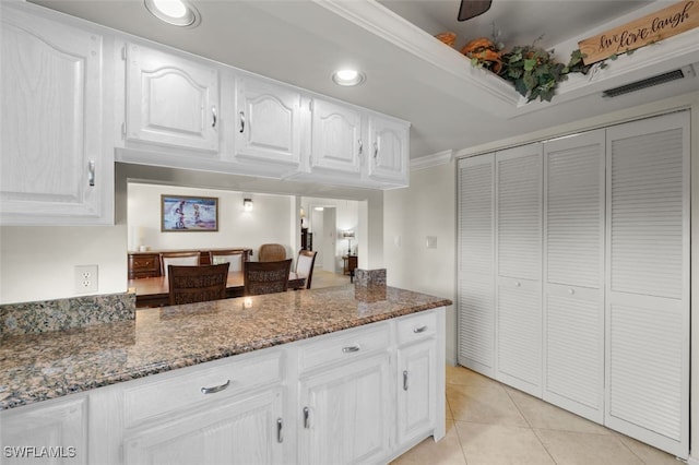 kitchen featuring white cabinets, light tile patterned floors, crown molding, and dark stone countertops