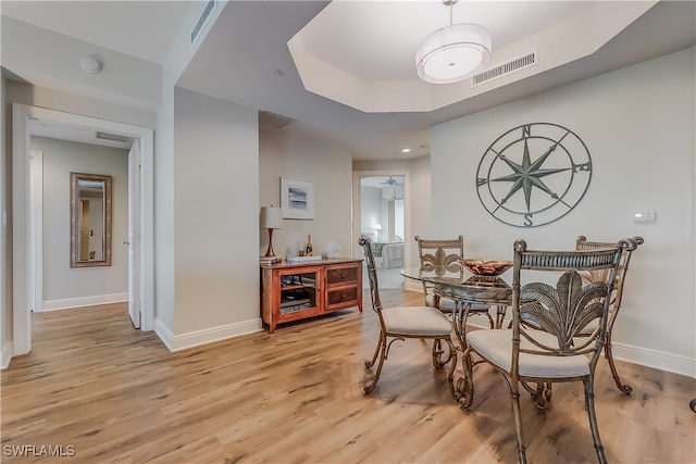 dining area with light wood-type flooring and a raised ceiling