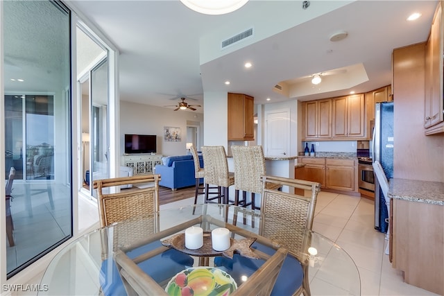 tiled dining space featuring ceiling fan and a raised ceiling