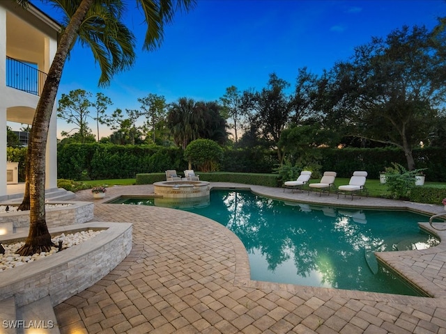 pool at dusk with a patio and an in ground hot tub