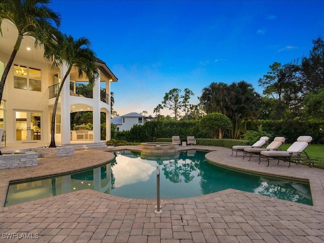 pool at dusk featuring a pool with connected hot tub and a patio area