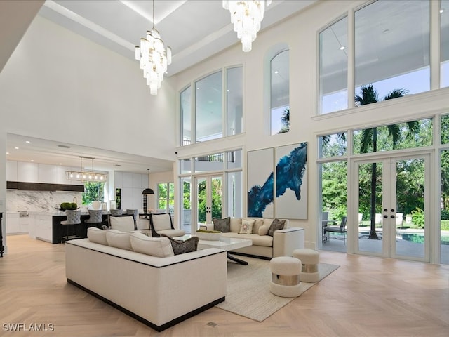 living room with light parquet floors, a towering ceiling, a chandelier, and french doors