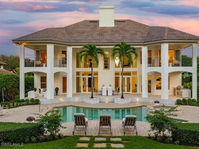 rear view of house with stucco siding, a patio, french doors, a balcony, and a chimney
