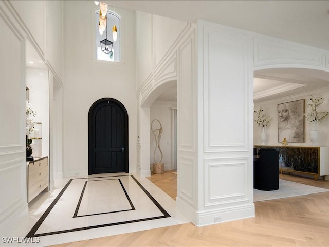 foyer featuring crown molding, a decorative wall, baseboards, arched walkways, and a towering ceiling