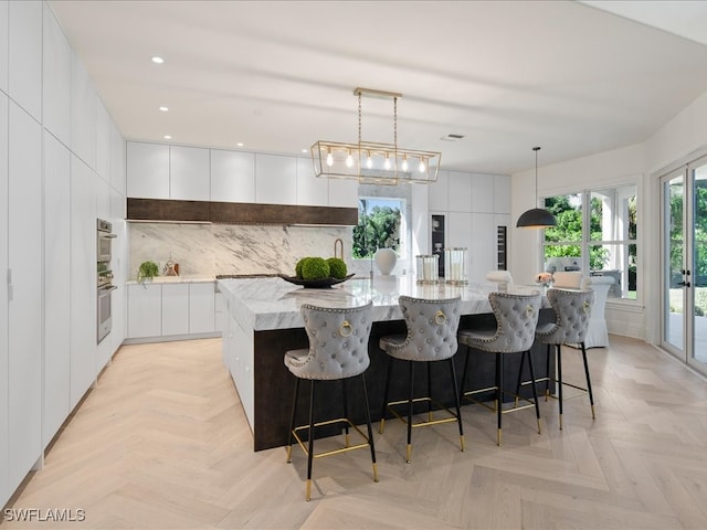 kitchen featuring a large island, white cabinetry, light parquet flooring, and hanging light fixtures