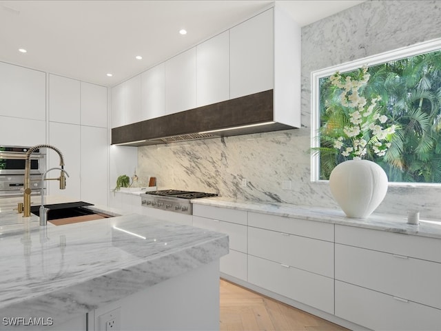 kitchen featuring light stone counters, white cabinets, stainless steel appliances, and light parquet floors