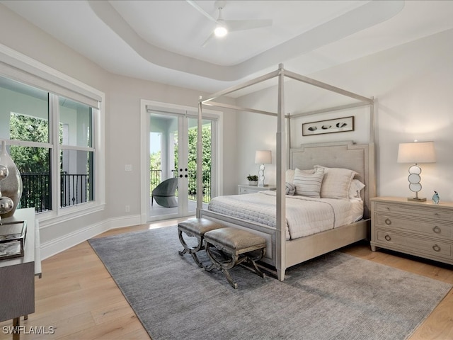 bedroom with ceiling fan, access to exterior, a tray ceiling, and light hardwood / wood-style floors