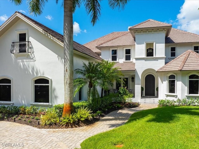 mediterranean / spanish house with a front lawn, stucco siding, and a tiled roof